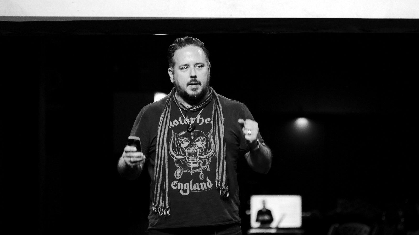 Jason Miller speaking on stage in a Motorhead T-shirt